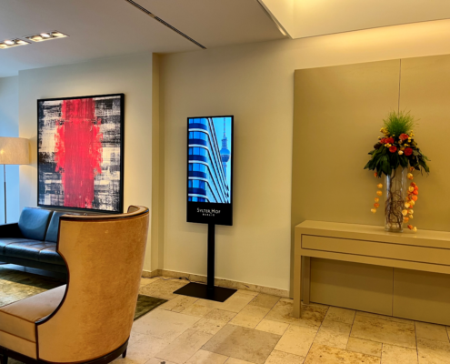 Digital_Screen_Hotel_Sylter_Hof_Berlin Digitaler Indoor-Werbescreen in einer modernen Hotellobby mit Sitzbereich, Kunstwerk und Blumenarrangement – Beispiel für digitale Werbung in Hotels.