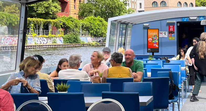 Digitaler Screen mit Werbung auf dem überdachten Deck eines Ausflugsschiffs.
